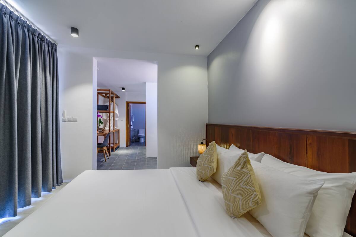 Habitación de hotel con una cama grande, cabecero de madera y vista al pasillo.