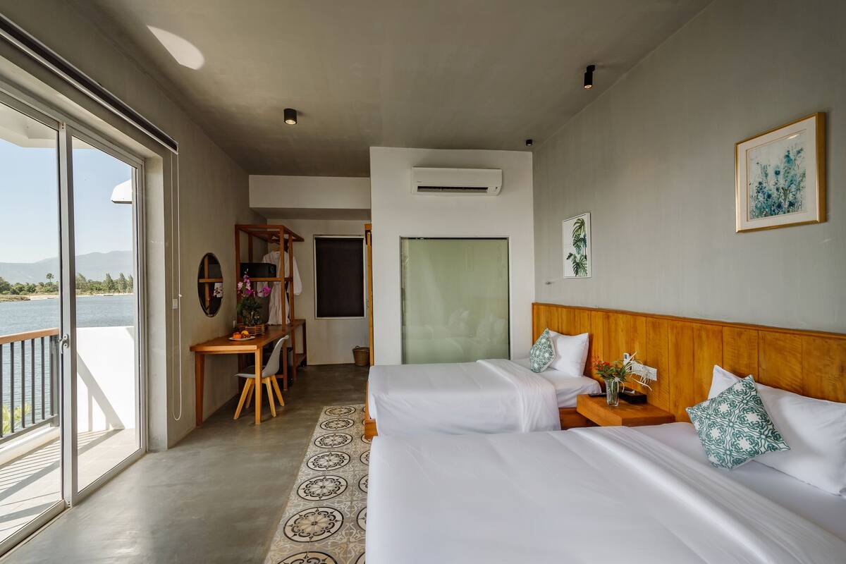 Habitación de hotel con dos camas, un escritorio y vista al agua.