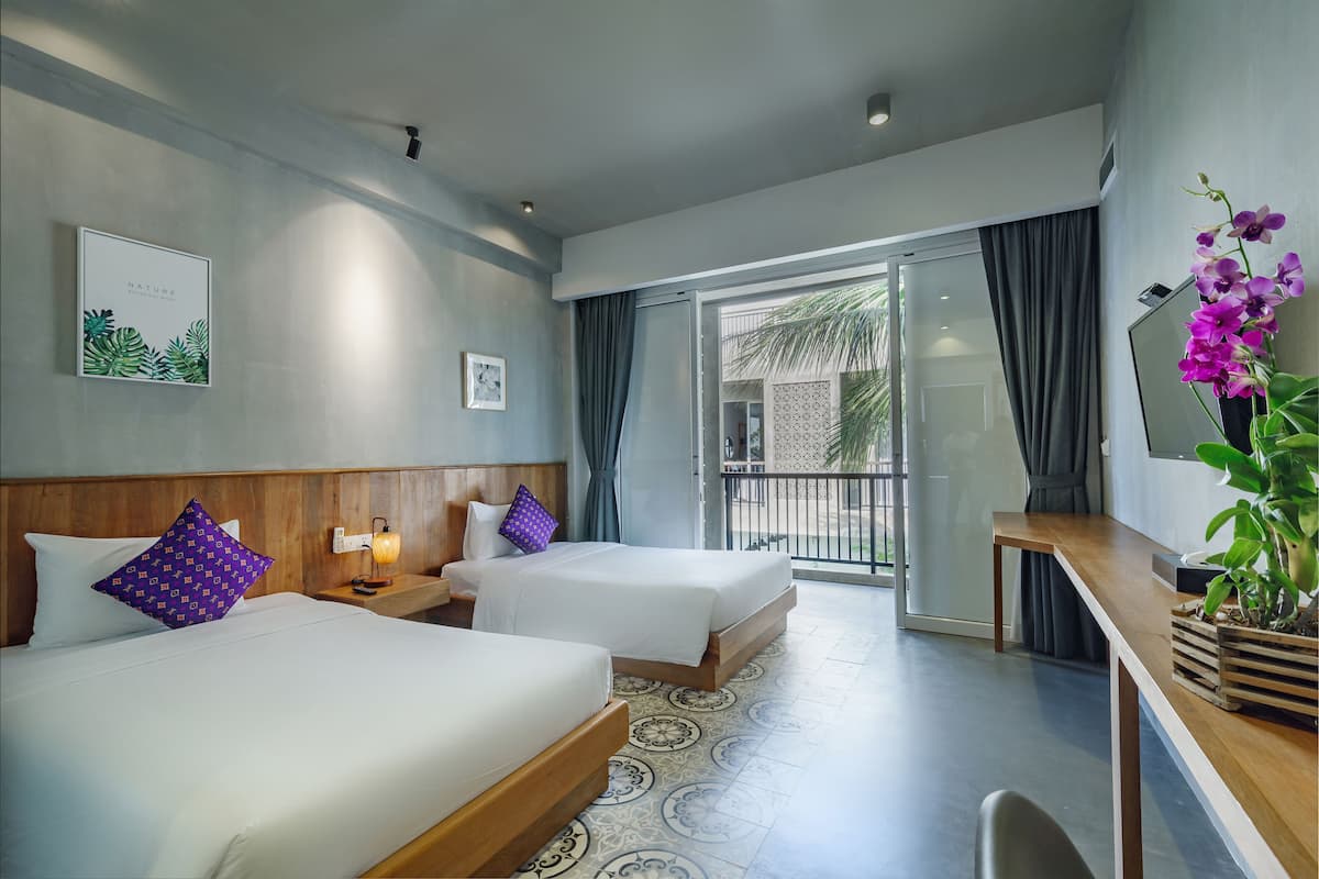 Habitación de hotel con dos camas, un escritorio y un balcón con cortinas.