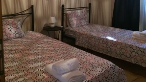A room with two single beds, a small table, a wall-mounted air conditioner, and a ceiling light fixture. - Leonidas Stone Houses Near Beach 50 Meters Away From Tavern With Local Food (West Mani)
