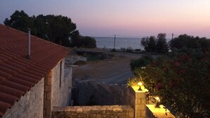 A coastal view with a stone building, a paved area, and a body of water in the distance. - Leonidas Stone Houses Near Beach 50 Meters Away From Tavern With Local Food (West Mani)