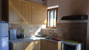 A compact kitchen with wooden cabinets, a built-in microwave, a coffee maker, and a window above the sink. - Leonidas Stone Houses Near Beach 50 Meters Away From Tavern With Local Food (West Mani)