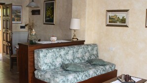 A living room with a sofa, a small table, and a lamp. There are framed pictures on the wall and a radiator in the background. - Holidays In The Heart Of Chianti Classico (Barberino Tavarnelle)