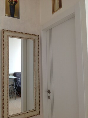 Una puerta blanca con un espejo grande que refleja una habitación con una silla y una mesa.