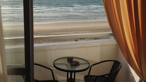 Un balcón con mesa y sillas de vidrio, con vista a una playa y al océano.
