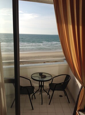 Un balcón con mesa y sillas de vidrio, con vista a una playa y al océano.