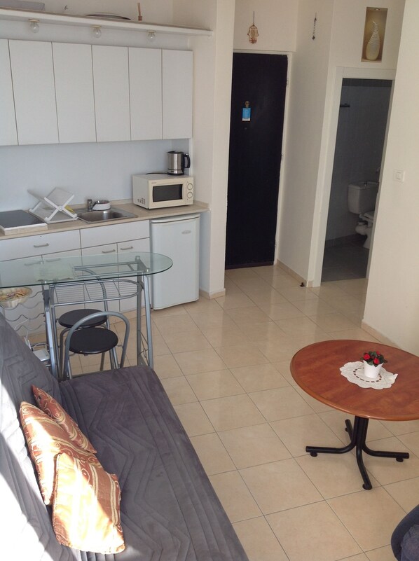 Un espacio habitable compacto con kitchenette, una zona de comedor y una pequeña mesa con un jarrón.