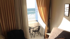 Una habitación con vista al océano, un sofá, una silla, una mesita y una lámpara.