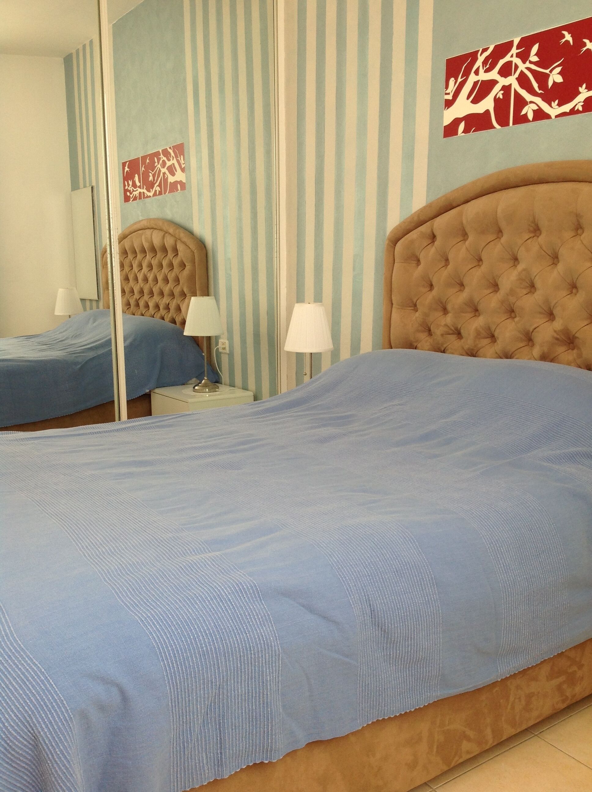A hotel room with a large bed, a smaller bed, a mirror, striped wallpaper, and a wall art piece.