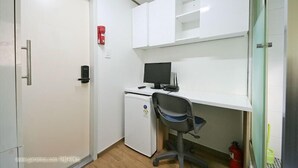 Un pequeño espacio de oficina con un escritorio blanco, una computadora, una silla, un refrigerador blanco y un extintor.