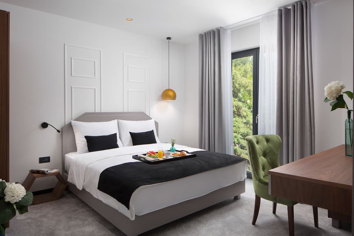 Ein modernes Hotelzimmer mit einem ordentlich bezogenen Bett, einem Frühstücksbrett und einem Essbereich mit Tisch und Stuhl.