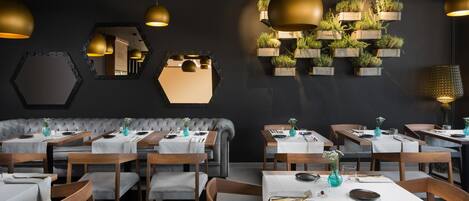 Interior de restaurante com espelhos hexagonais, mesas e cadeiras de madeira, e um arranjo de plantas na parede.