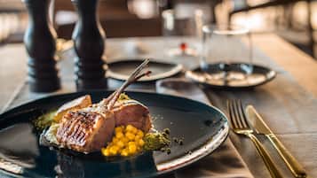A plate with a piece of meat, corn, and green garnish on a dark plate.