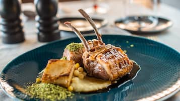 Une assiette contenant un plat de jarret d’agneau, des pommes de terre et une garniture de légumes verts.