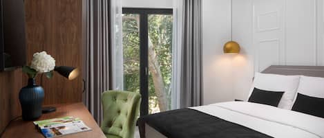 Una habitación de hotel con cama, escritorio con lámpara, silla, jarrón con flores y ventana con cortinas.