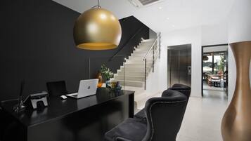 A modern reception desk with a laptop, a vase, and a potted plant. A staircase leads to an upper level.