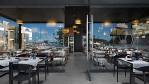 Un restaurante espacioso con múltiples mesas y sillas, ventanas amplias que ofrecen vistas al puerto y moderna iluminación colgante.