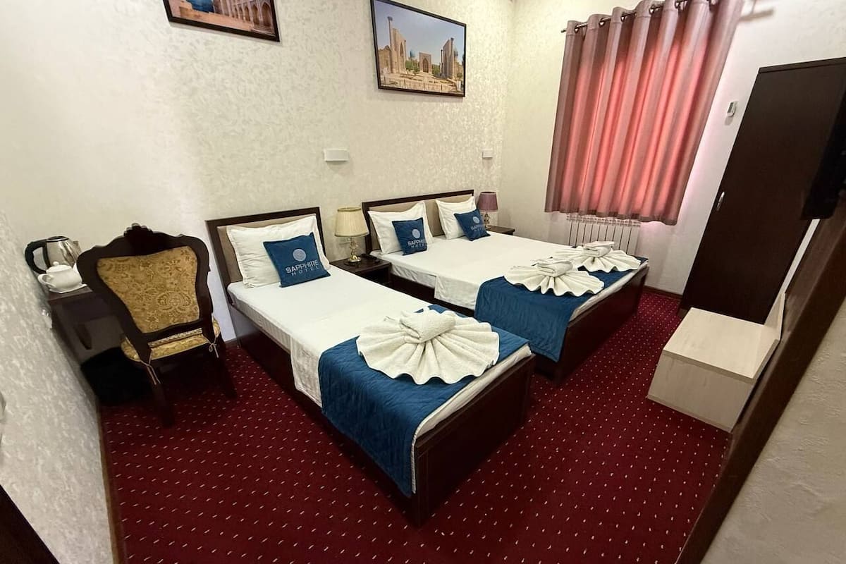 A hotel room with two beds, a chair, a desk, and a television.