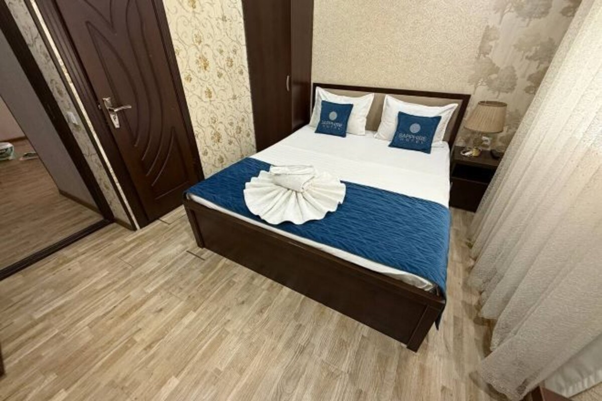 A neatly made bed with a blue bedspread and white pillows, a wooden headboard, and a nightstand with a lamp.