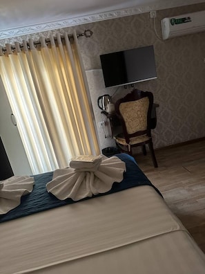 A hotel room with a bed, curtains, a television, a chair, and an air conditioning unit.
