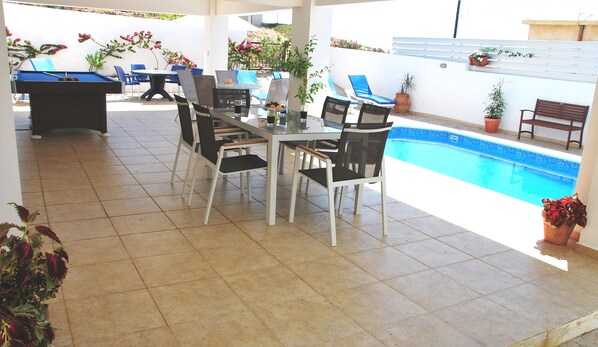 A covered patio with a pool, a dining table with chairs, and a pool table.