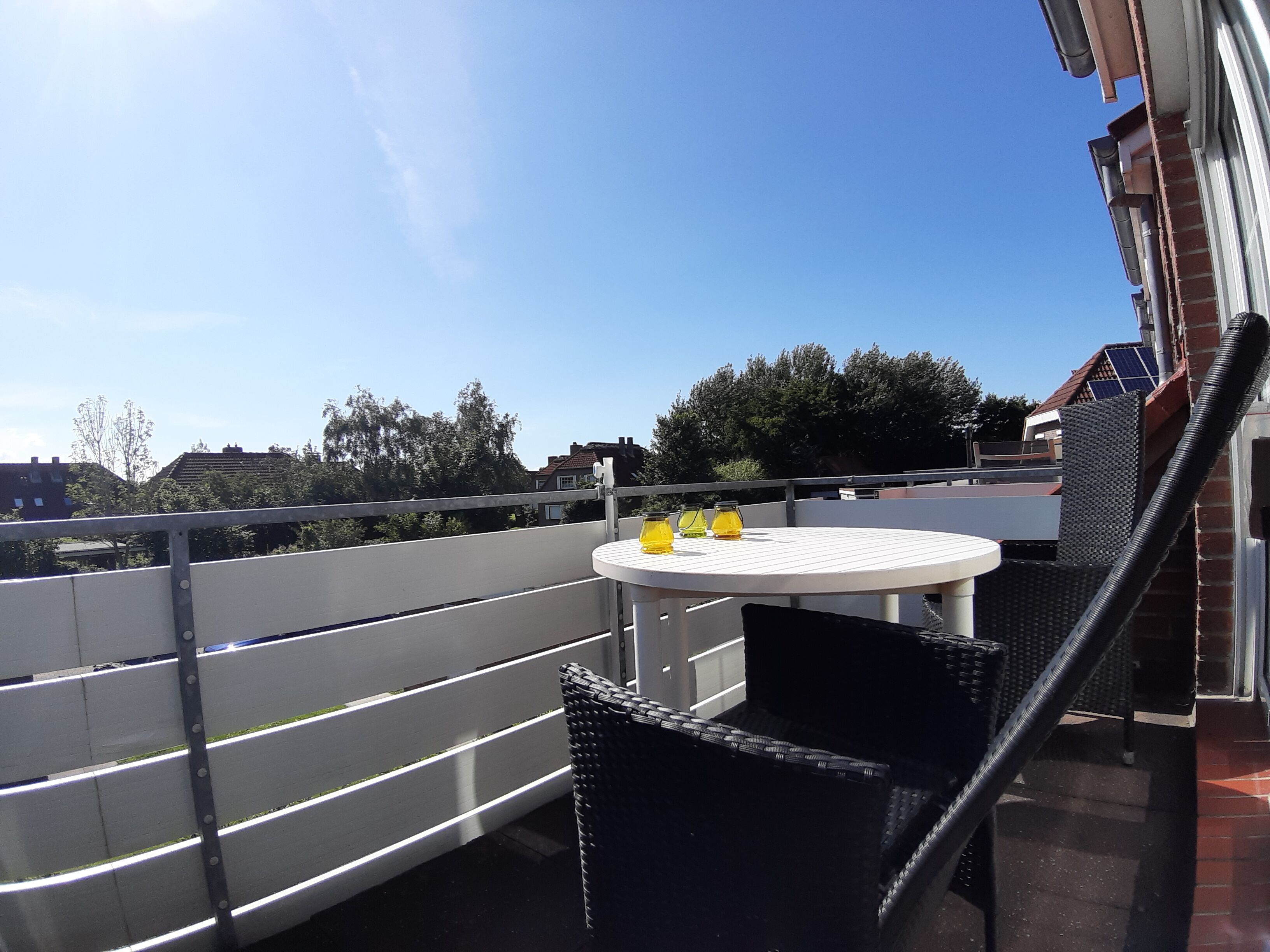 A rooftop terrace with a round table and chairs, a railing, and a view of the cityscape.