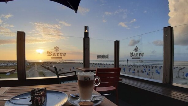 A table with a dessert and a glass of beer, overlooking a beach with 'Barre' signage.
