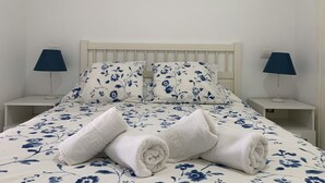 Una cama bien hecha con ropa de cama floral, dos lámparas de noche y un cuadro con una playa sobre la cama.