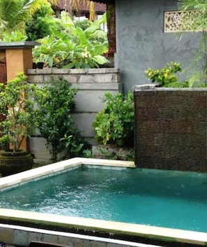 A rectangular swimming pool with a stone border, surrounded by lush greenery and a stone wall. - Gardenia Gardensbest Breakfast in Bali (Ubud)