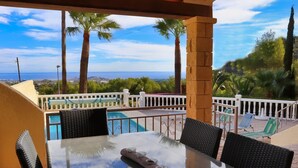 Eine Terrasse mit Glastisch, Stühlen und Blick auf das Meer und Palmen.