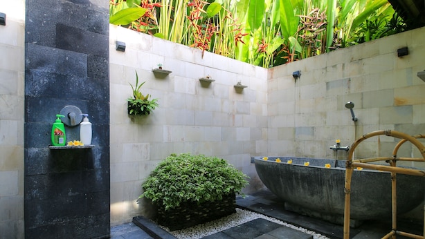 A modern bathroom with a freestanding bathtub, a small shelf with toiletries, and a potted plant. - Bungalow Jepunbest Breakfast in Bali (Ubud)