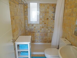 Une salle de bain avec une baignoire, des toilettes et une fenêtre située au-dessus de la douche.