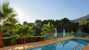 A rectangular swimming pool with a tiled deck, surrounded by palm trees and a metal fence. - Casa Casaert - Altea, Costa Blanca (Altea)