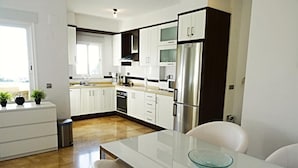 A modern kitchen with white cabinets, stainless steel appliances, and a glass-top dining table. - Casa Casaert - Altea, Costa Blanca (Altea)