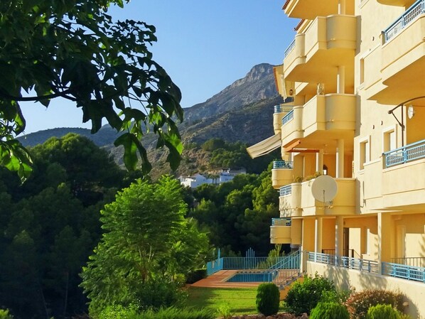 Un bâtiment jaune doté de balcons, entouré de verdure et de montagnes.
