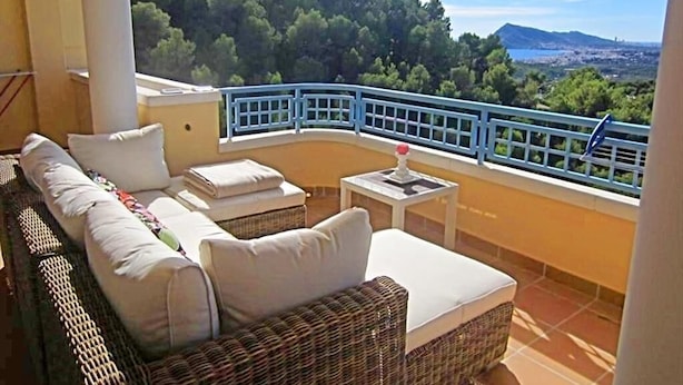 A balcony with wicker furniture, a small table, and a view of a forested area and distant landscape. - Casa Casaert - Altea, Costa Blanca (Altea)