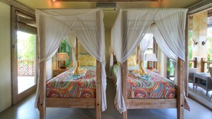A room with two wooden four-poster beds with white canopies, colorful bedding, bedside lamps, and a view of greenery outside. - Hibiscus Guest Suitebest Breakfast in Bali (Ubud)