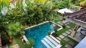 A rectangular swimming pool surrounded by lush greenery, with a patio area featuring a table and chairs. - Hibiscus Guest Suitebest Breakfast in Bali (Ubud)