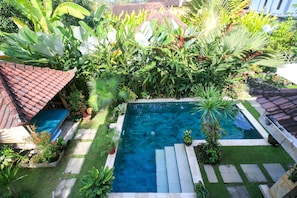 A rectangular swimming pool surrounded by lush greenery and a tiled roof structure. - Hibiscus Guest Suitebest Breakfast in Bali (Ubud)