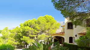 Une villa de style méditerranéen avec piscine, entourée d’une végétation luxuriante et avec des montagnes en toile de fond.