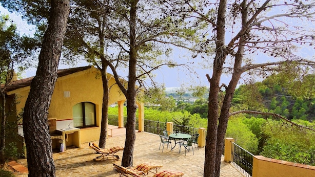 Une terrasse avec un sol en pierre, un bâtiment jaune et une vue sur des collines verdoyantes.