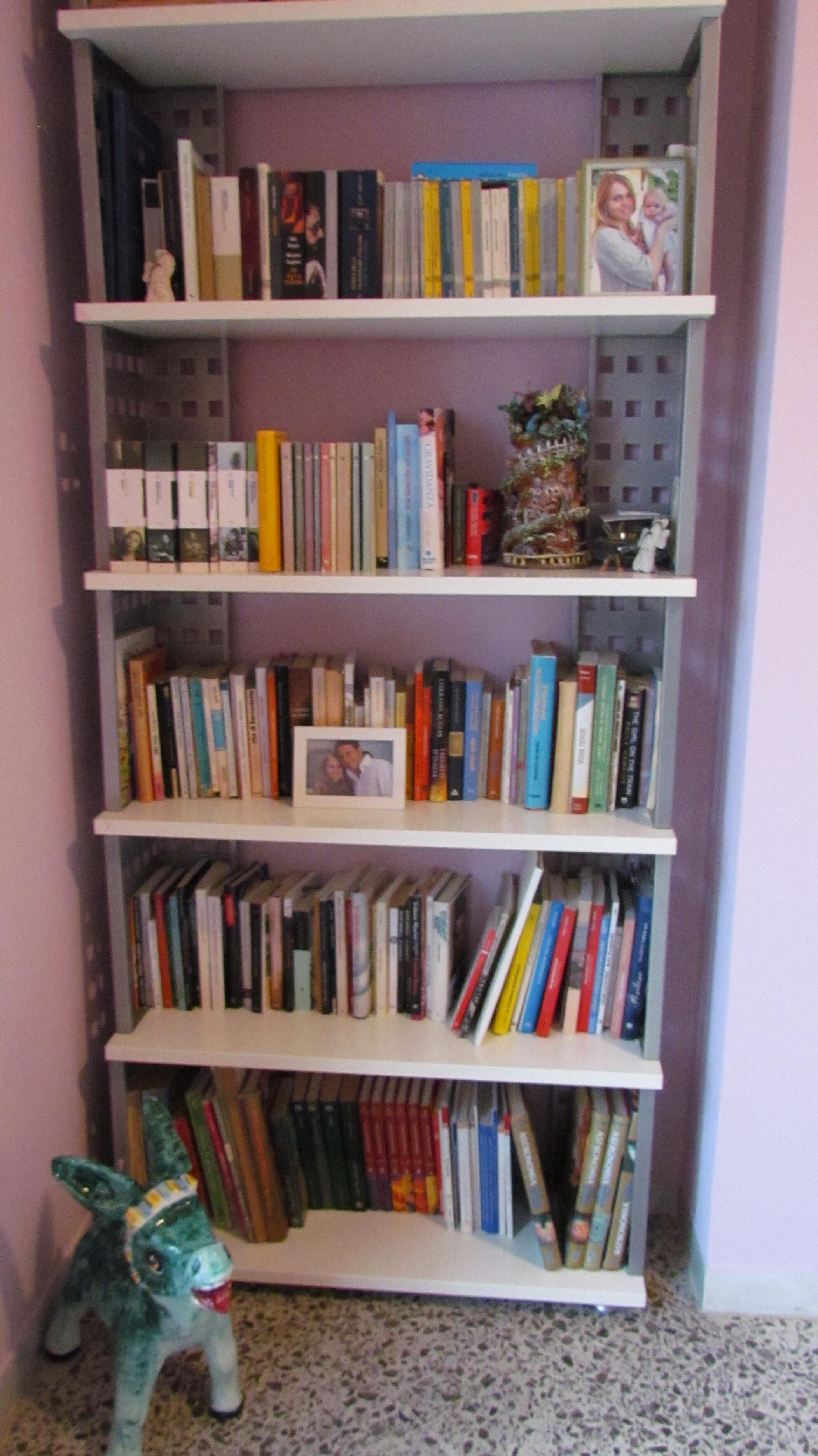Uma estante com várias prateleiras cheias de livros, um pequeno objeto decorativo e uma figurina.