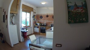 A kitchen with a window, a dining area with a glass table, and a painting on the wall. - Wonderful Amalfi Coast Apartment Overlooking the sea With Free Wifi and Parking (Vietri sul Mare)