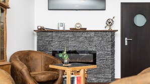 A living room with a stone fireplace, a television mounted above it, and a door with a round glass panel. - Hotel Köln 2020 (Cologne)