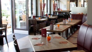 A restaurant with wooden tables and chairs, a glass door entrance, and a view of the street outside. - Hotel Köln 2020 (Cologne)