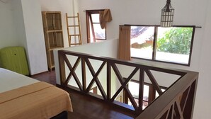 A bedroom with a bed, a wooden railing, a window with curtains, and a view of greenery outside. - Frog House a Charming Apartment in Best Bali Location (Seminyak)