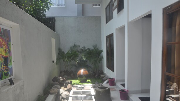 A narrow courtyard with a water feature, potted plants, and a large vase. - Frog House a Charming Apartment in Best Bali Location (Seminyak)