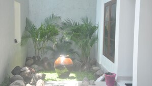 A small garden area with a large terracotta pot, palm trees, and rocks. - Frog House a Charming Apartment in Best Bali Location (Seminyak)