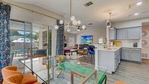 Una cocina moderna con armarios grises, una isla central y una zona de comedor con sillas naranjas y una mesa de vidrio.