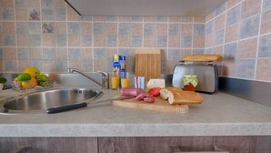 A kitchen with a sink, a cutting board with food items, a toaster, and a fruit basket. - Vistonia Studio 5 Directly on the Beach With sea View (Corfu)